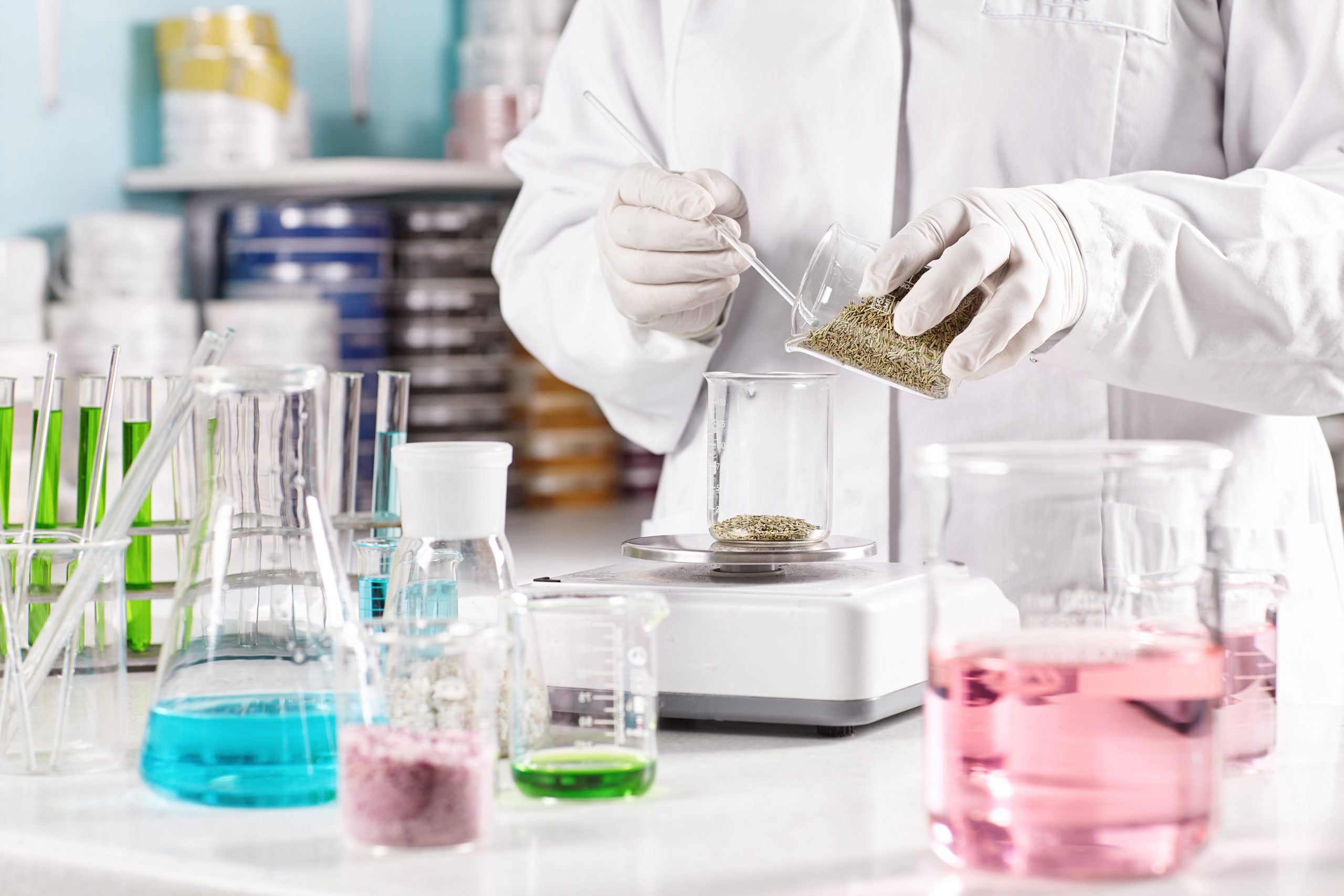 Scientific research at laboratory on finding out new species of vegetation. Researcher in white gown standing near all his equipment analyzing process, weighting seeds on scales in glass container